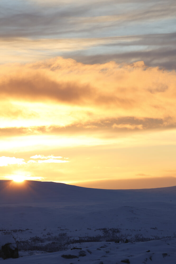 Aurinko laskee lumisen tunturin taakse