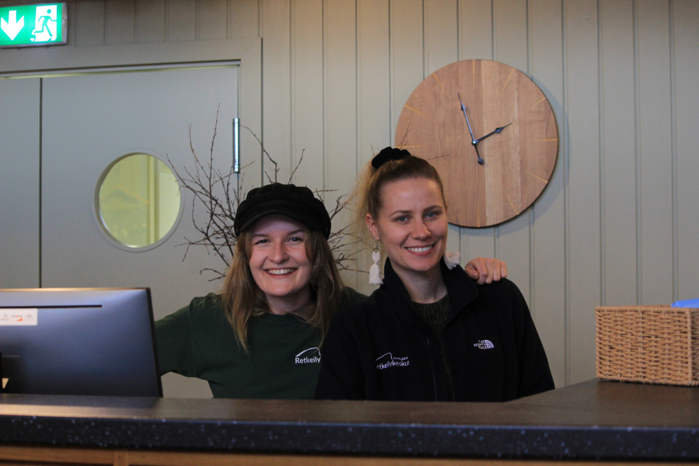 Kaksi naista Kilpisjärven Retkeilykeskuksen vastaanottotiskin takana hymyilee 