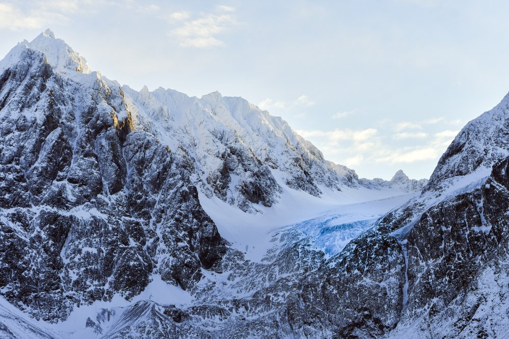 Lumihuippuisten vuorten keskellä sinisenä hohtava jäätikkö