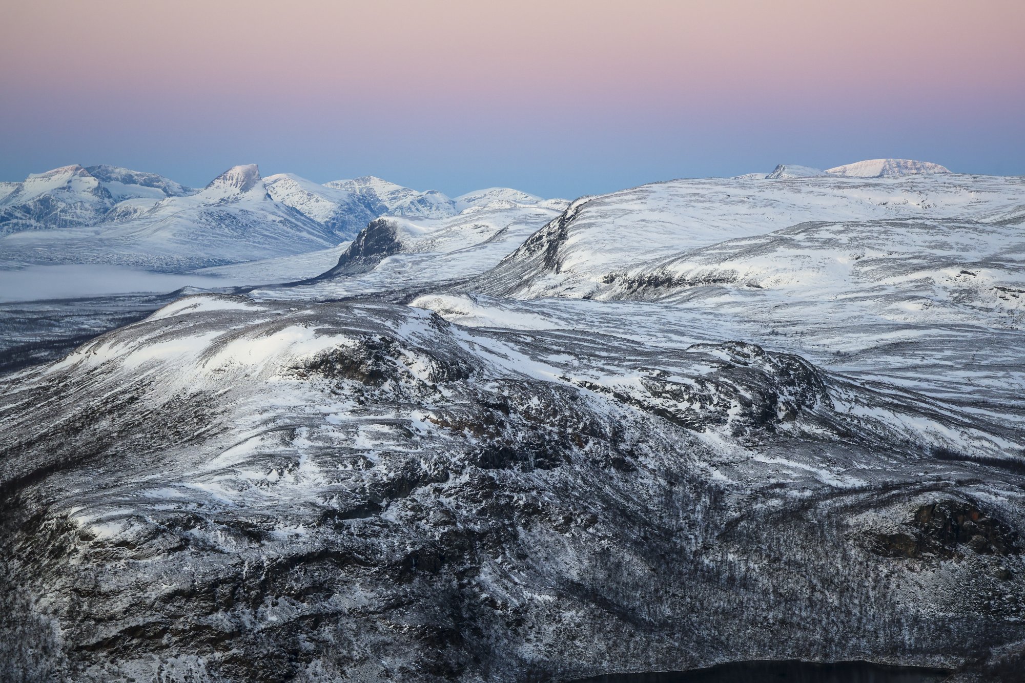 Maisemaa Saanalta kohti Norjaa. Taivas on pastellinsävyinen, tuntureilla on hiukan lunta.