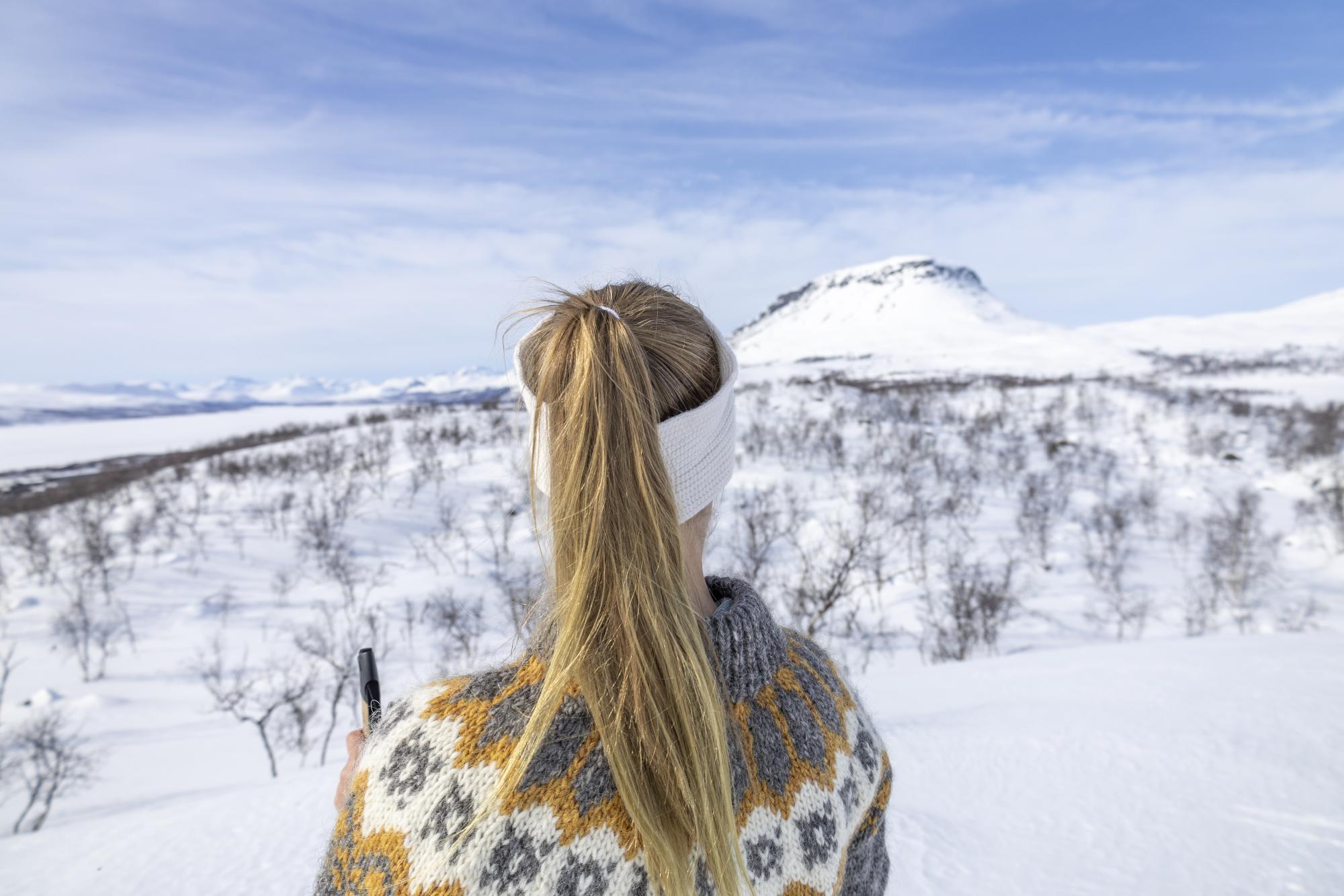 Nainen villapaidassa katselee aurinkoista kevätmaisemaa kohti saana-tunturia Kilpisjärvellä