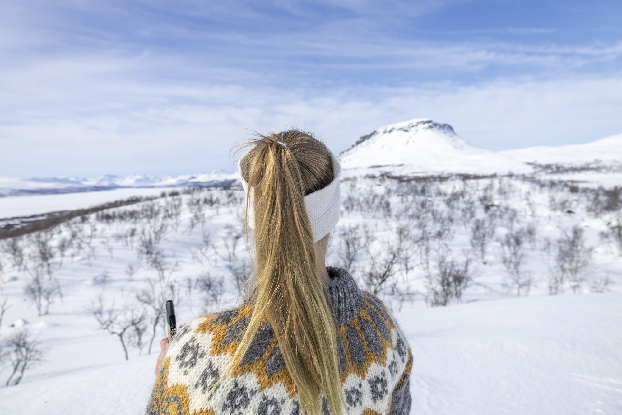 Nainen villapaidassa katselee aurinkoista kevätmaisemaa kohti saana-tunturia Kilpisjärvellä