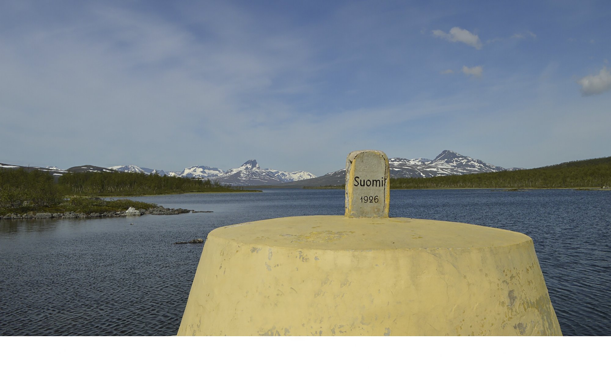 Rajapyykki Kolmen valtakunnan rajalla taustalla lumisia vuoria Norjan puolella