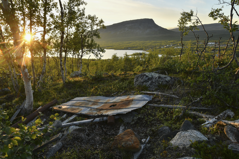 Sodanaikaisen leirin jäänteet Salmivaaran laidalla laskevan auringon valossa. Kuvassa on erilaisia ruostuneita metallinosia. 