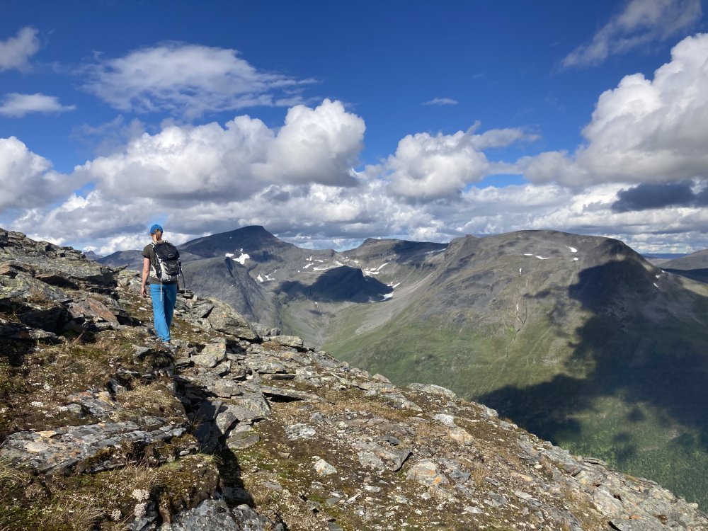 Ylhäällä jylhän vuoren rinteellä nainen kävelee reppu selässään kesäpäivänä