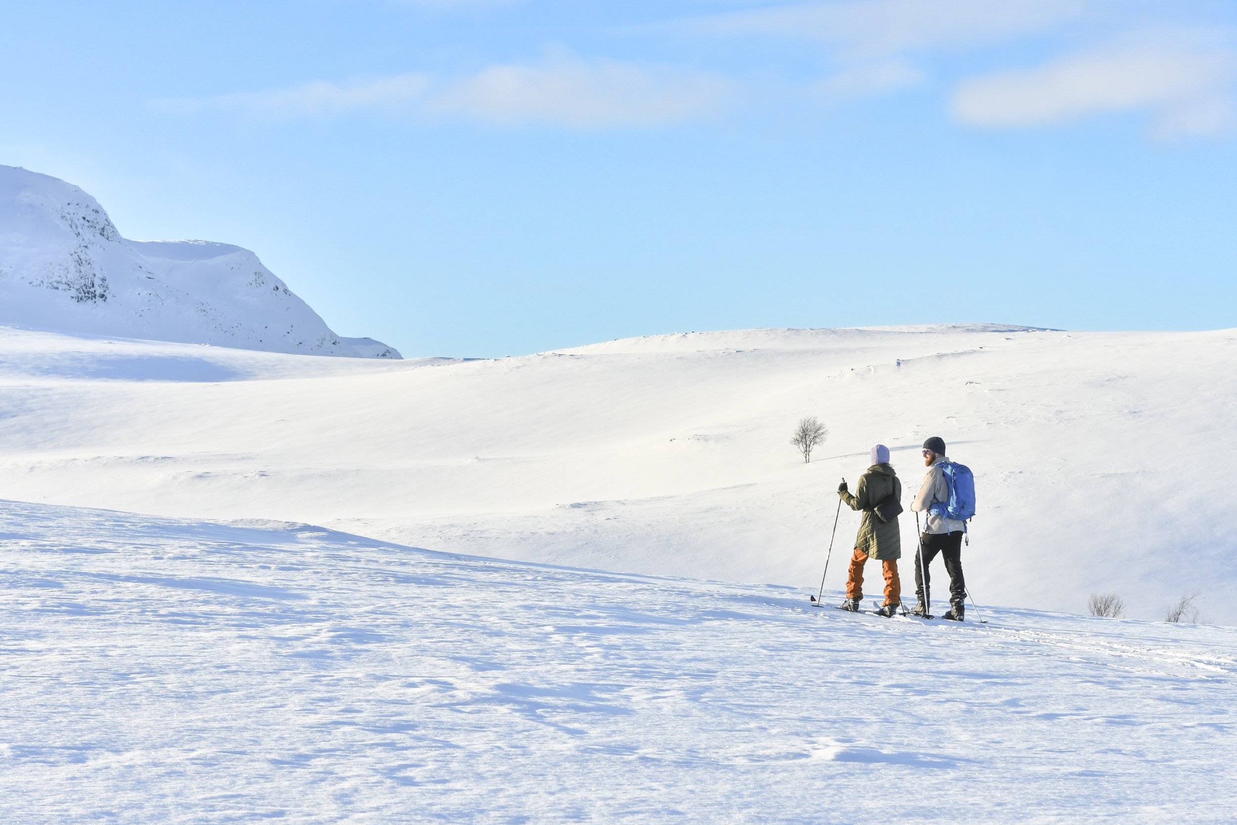 Kaksi ihmistä hiihtää Kilpisjärven Retkeilykeskukselta vuokratuilla suksilla kilpisjärven aurinkoisilla keväthangilla