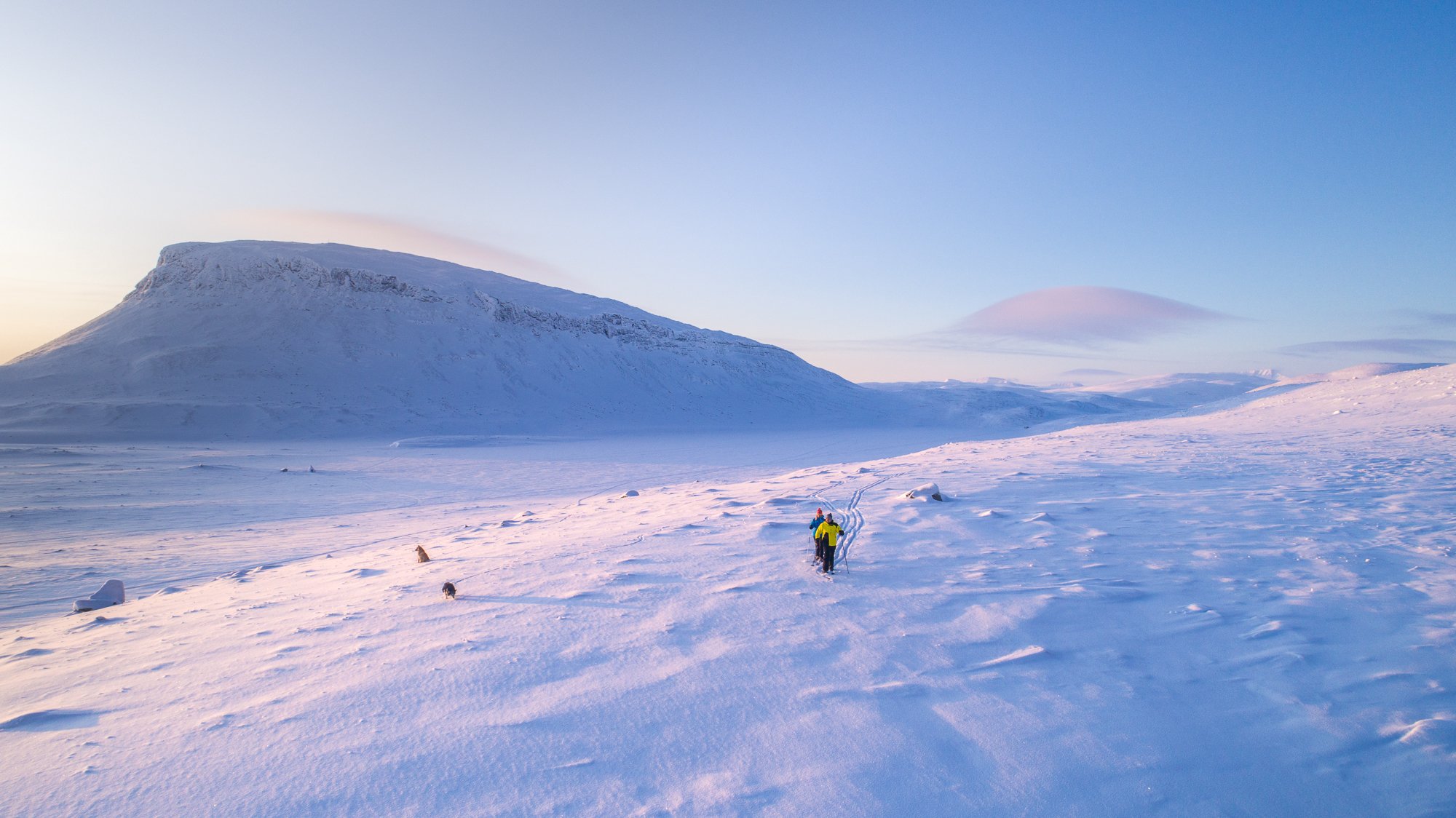 Kaksi ihmistä hiihtää tunturisuksilla Saanatunturin laidalla auringonlaskun aikaan