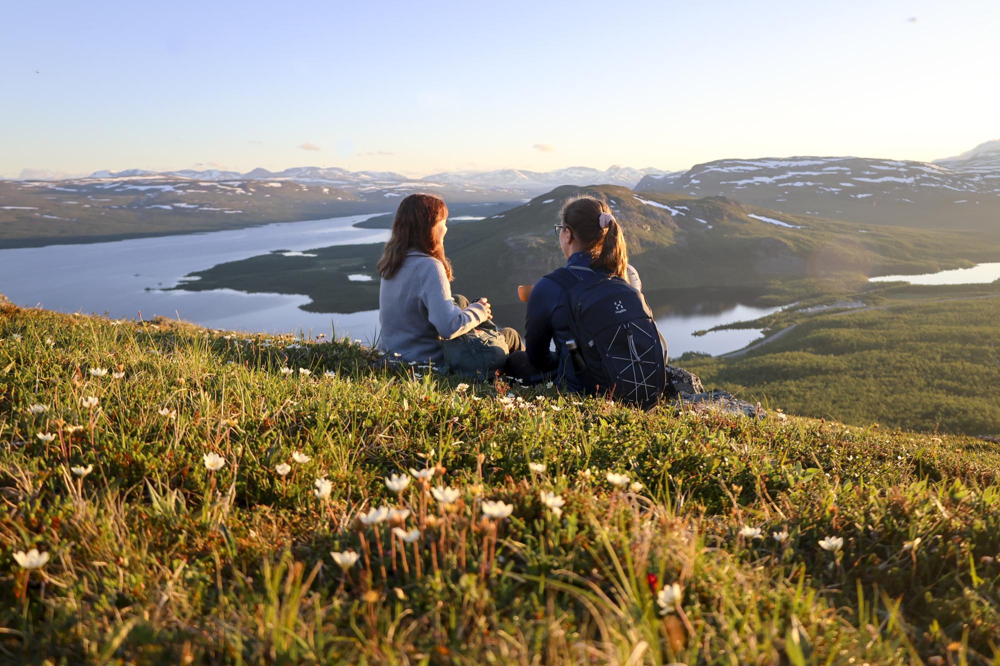 Kaksi naista retkeilee ja juo kahvia Kilpisjärven Retkeilykeskukselta lähtevällä polulla, Saanan rinteellä aurinkoisena kesäyönä. 
