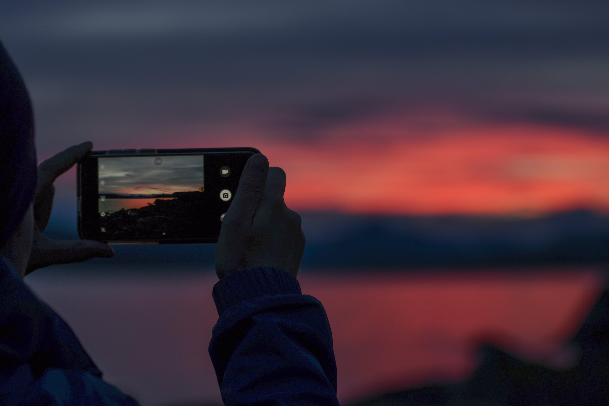 Nainen valokuvaa puhelimella värikästä auringonlaskua Kilpisjärvellä
