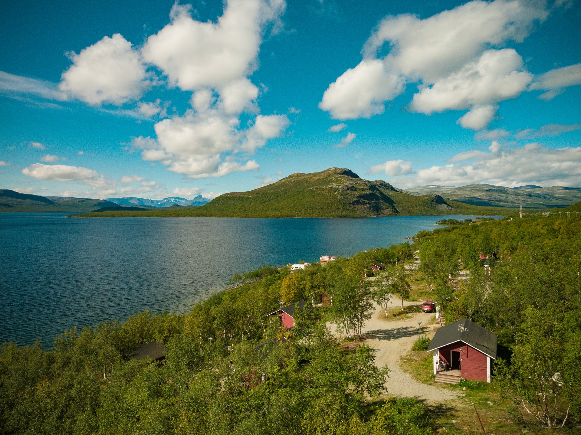 Kilpisjärven Retkeilykeskuksen mökit Kilpisjärven rannalla kesäisenä päivänä, pikku-Malla kauniina järven toisella puolella. 
