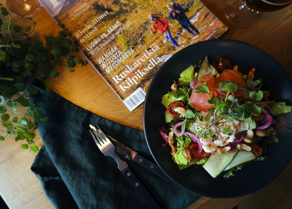 Lohisalaattiannos Kilpisjärven Retkeilykeskuksen ravintolan pöydällä. Pöydällä on myös avoin lehti, haarukka, servetti sekä vihreä kasvi.