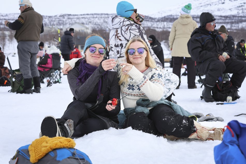 Kaksi naista osallistuu Kilpisjärven Vain kaksi kalaa tapahtumaan ja istuvat avannon reunalla hymyillen kameraan villapaidoissaan.