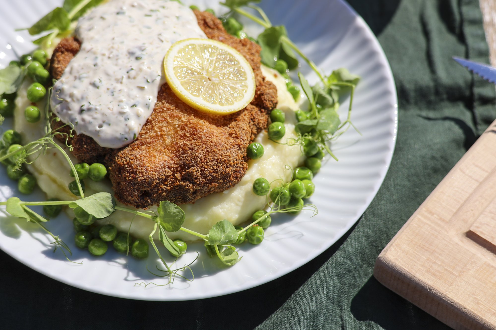 Kuvassa on valkoisella lautasella haukiwallenberg. Annoksessa on perunamuusia ja herneitä, lautanen on Kilpisjärven Retkeilykeskuksen ravintola Saanan pöydällä terassilla aurinkoisena kesäpäivänä.