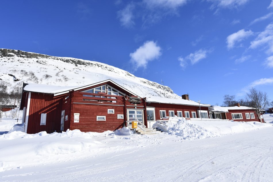 Kilpisjärven Retkeilykeskuksen punainen päärakennus Saanan juurella valkoisten hankien keskellä aurinkoisena kevätpäivänä